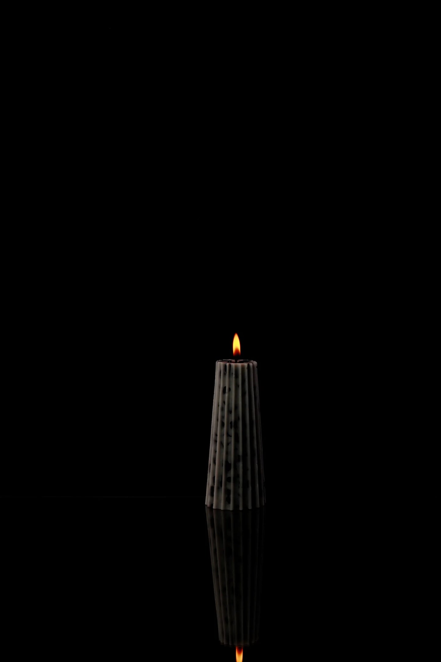 A large tapered okra fruit-inspired candle with internal chips, that can also tie resemblance to a gear.